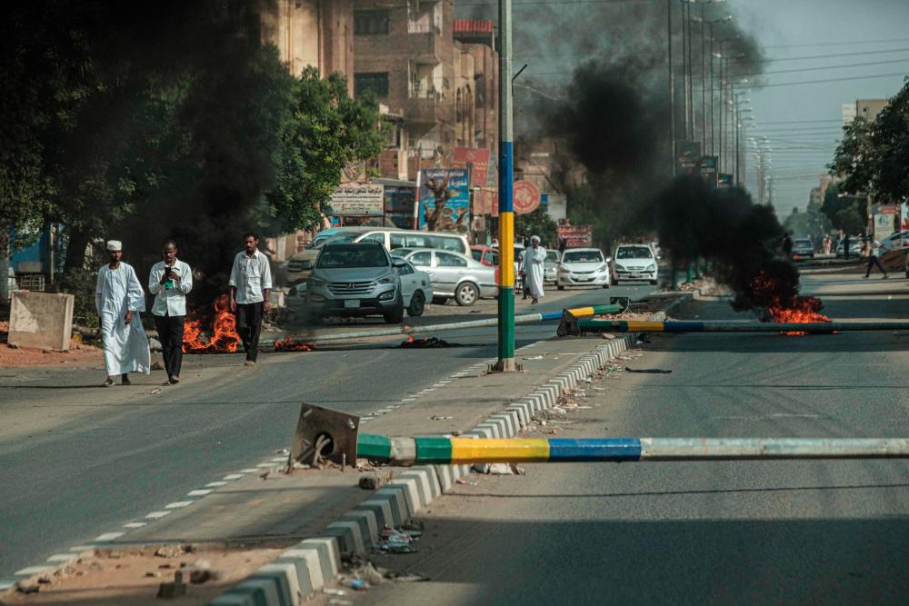 People walk past burning tires after protesters set fire and pulled down street light polls on a street, in the capital Khartoum's twin city Omdurman, on June 21, 2019. - AFP