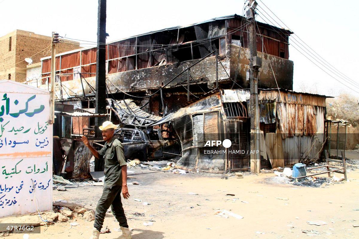 A Sudanese army soldier waves as he walks past a war-damaged building in Salha, south of Omdurman, two days after the Sudanese army recaptured it from the paramilitary Rapid Support Forces (RSF), on May 22, 2025. - Ebrahim Hamid / AFP
