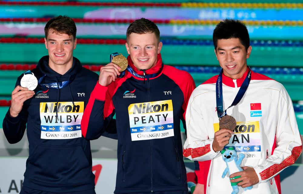 (L-R) Silver medallist Britain's James Wilby, gold medallist Britain's Adam Peaty and bronze medallist China's Yan Zibei celebrate during the medals ceremony after the final of the men's 100m breaststroke event during the swimming competition at the 2019 World Championships at Nambu University Municipal Aquatics Center in Gwangju, South Korea, on July 22, 2019. — AFP
