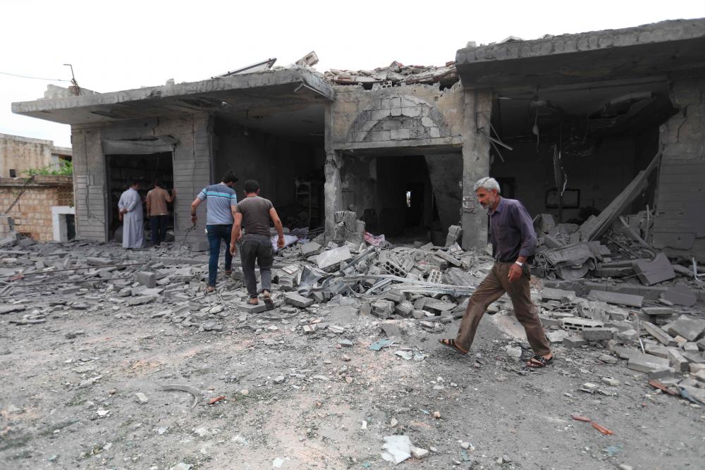 People walk past destruction at the scene of an area targeted by regime airstrikes in the village of Kafr Aweid in which five people were killed, including two children on June 5, 2019 in the Syria's northern Idlib province. - AFP
