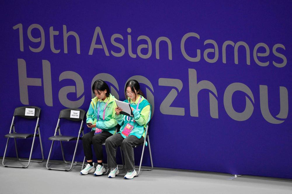 Volunteers sit in front of a sign of the Hangzhou Asian Games in the women's team preliminary round of table tennis during the 2022 Asian Games in Hangzhou//AFPix