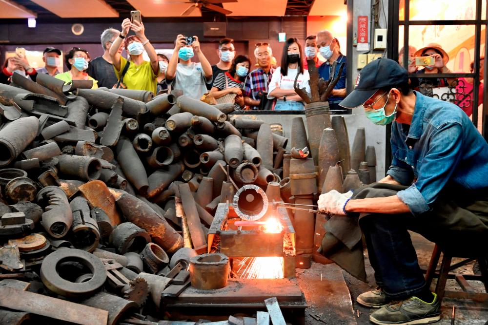 This photo taken on October 21, 2020 shows Taiwanese blacksmith Wu Tseng-dong (R), owner of a knife factory, giving a demonstration to tourists how to make a knife from cases of Chinese artillery shells which were fired decades ago from Xiamen on the mainland at Taiwan’s Kinmen island - which lies off the coast of the Chinese mainland. AFP / Sam Yeh