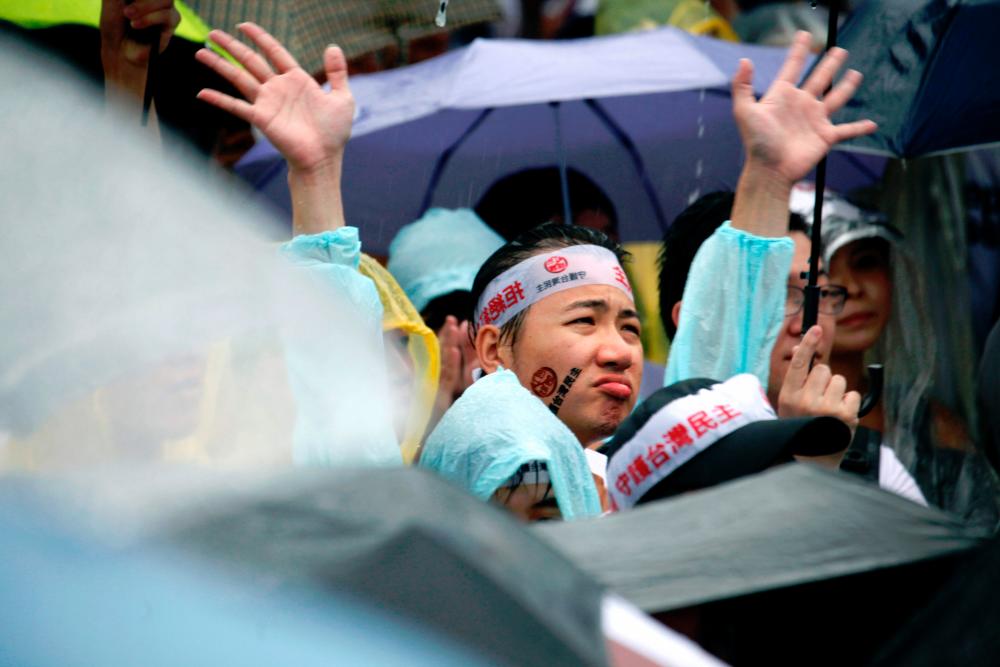 Protesters gather in the rain during a rally against pro-China media in front of the Presidential Office building in Taipei. — AFP