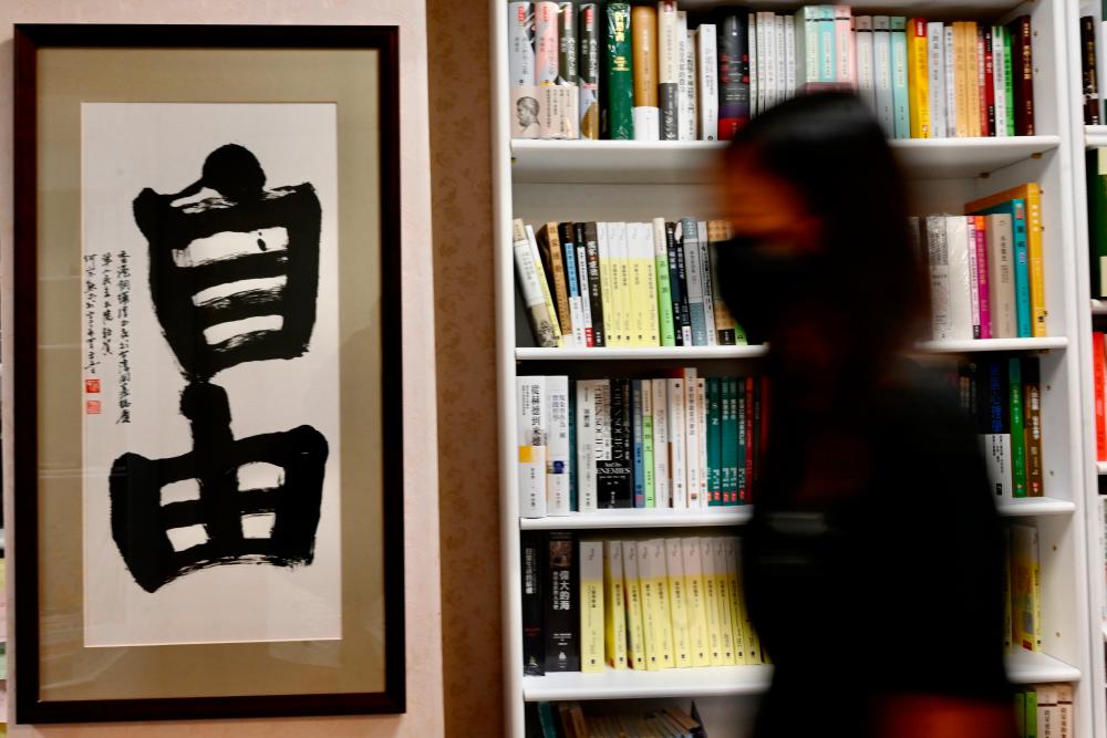 This photo taken on May 28, 2020 shows Xiao Hua of Hong Kong, a 35-year-old registered nurse who worked as a medic during the early stages of the protests in 2019, walking past calligraphy (L) on display reading “freedom” at the “Causeway Bay Books” bookstore, a shop set up by a Hong Kong dissident bookseller in Taipei. — AFP