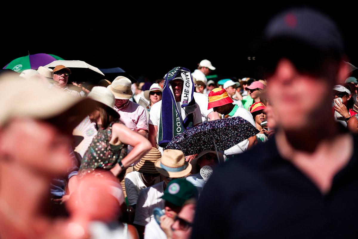A member of the public cover his head with towel to protect himself from the sun as he watches the men's singles first round tennis match between Spain's Carlos Alcaraz and Italy's Fabio Fognini on the first day of the 2025 Wimbledon Championships at The All England Lawn Tennis and Croquet Club in Wimbledon, southwest London, on June 30, 2025. - AFPPIX