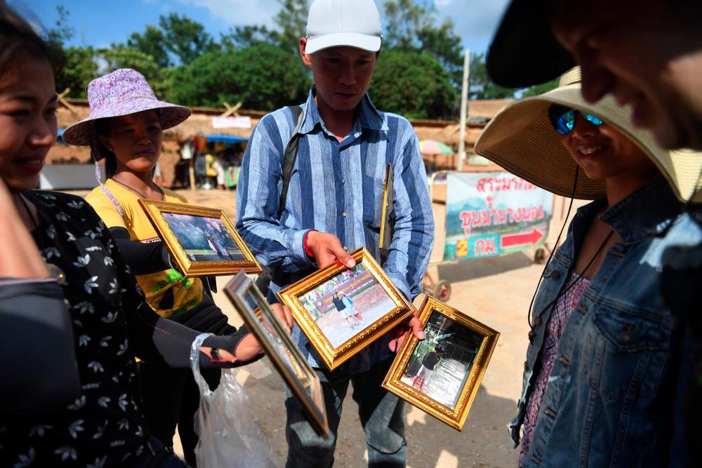 This picture taken on June 13, 2019 shows vendors selling souvenir photos on the road leading to the Tham Luang cave, in which 12 boys from the “Wild Boars” football team and their coach were trapped last year, in the Mae Sai district of Chiang Rai province. — AFP
