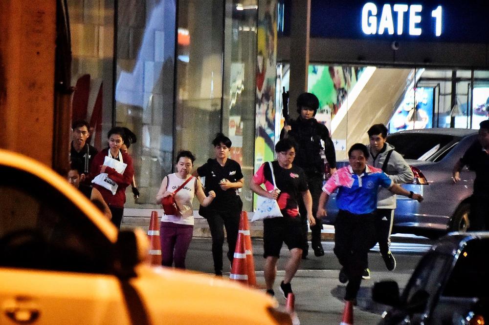 People run together as they are rescued by Thai commandos from Terminal 21 shopping mall, where a mass shooting took place, on Feb 9, 2020 in the Thai northeastern city of Nakhon Ratchasima. – AFP