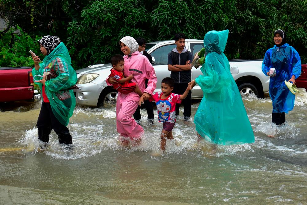 Women wear rain ponchos as they walk with children through floodwaters following heavy rain in Thailand’s southern province of Narathiwat on December 25, 2023/AFPPix