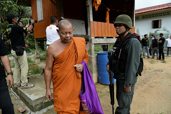 A Buddhist monk walks past an armed Thai police securing the compound of Rattanaupap temple in Narathiwat province on Jan 19, 2019 following an attack by black-clad gunmen that killed two Buddhist monks. — AFP