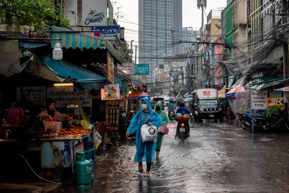 People wearing plastic ponchos walk along a flooded street following a heavy downpour of rain in Bangkok/AFPPix