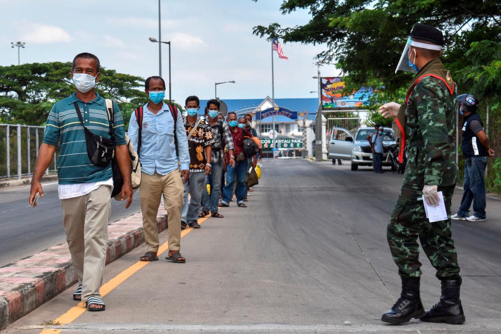 Thai people wearing face shields and face masks who returned to their hometown due to the spread of the coronavirus disease (Covid-19) walk in line at the Thai-Malaysia border in Narathiwat, Thailand, on April 18, 2020. - Reuters