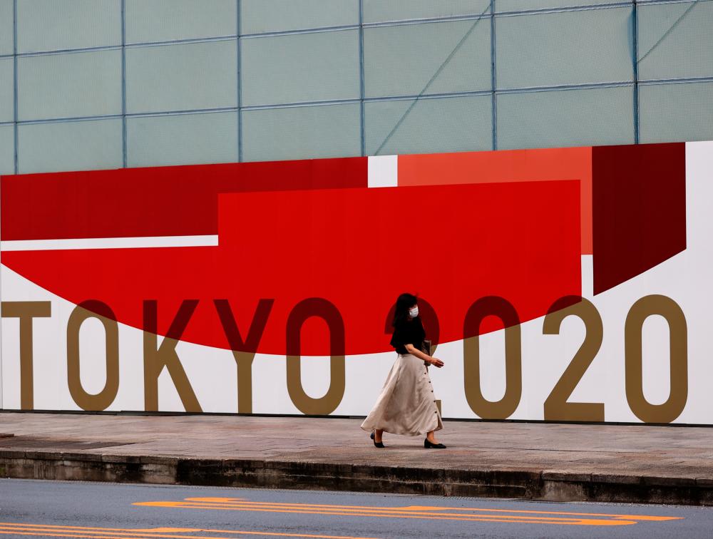 A woman, wearing a protective mask against Covid-19, walks past a wall bearing logo of Tokyo 2020 Olympic Games in Tokyo, Japan, July 29, 2021. — Reuters