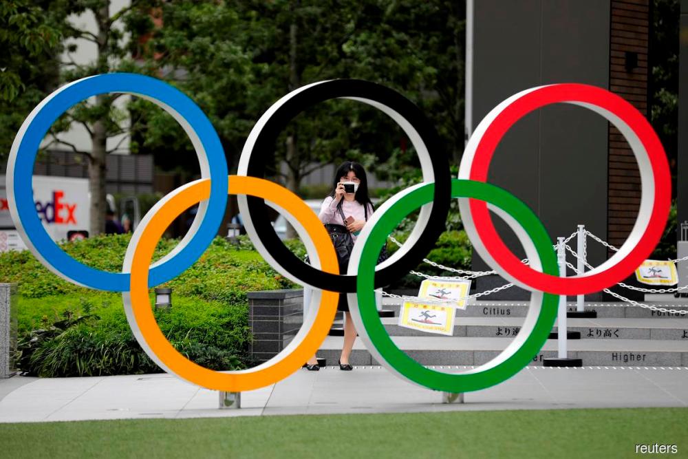A woman wearing a protective mask amid the coronavirus disease (Covid-19) outbreak, takes a picture of the Olympic rings in front of the National Stadium in Tokyo, Japan October 14, 2020. — Reuters