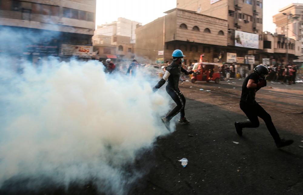 An Iraqi protester returns a tear gas canister thrown by security forces during clashes with them in the capital Baghdad's Khallani square during ongoing anti-government demonstrations on November 13, 2019. - AFP