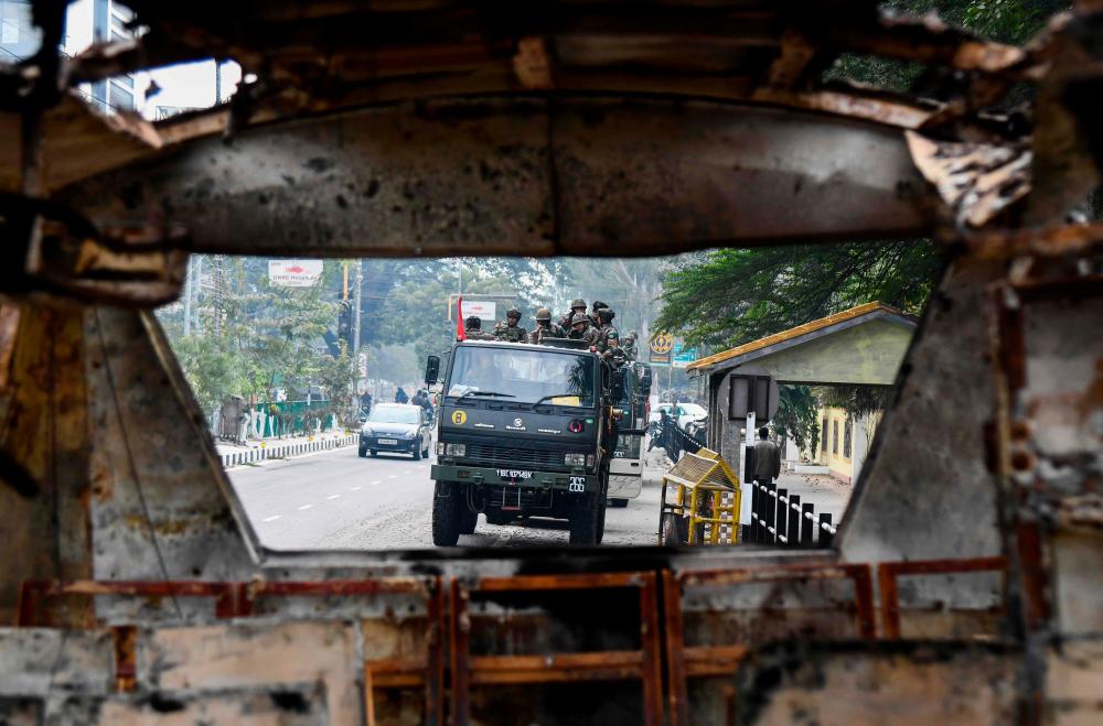 Soldiers are seen through the wreckage of a vehicle which was set on fire by demonstrators during a protest against the government's Citizenship Amendment Bill (CAB) in Guwahati on December 13, 2019. - AFP