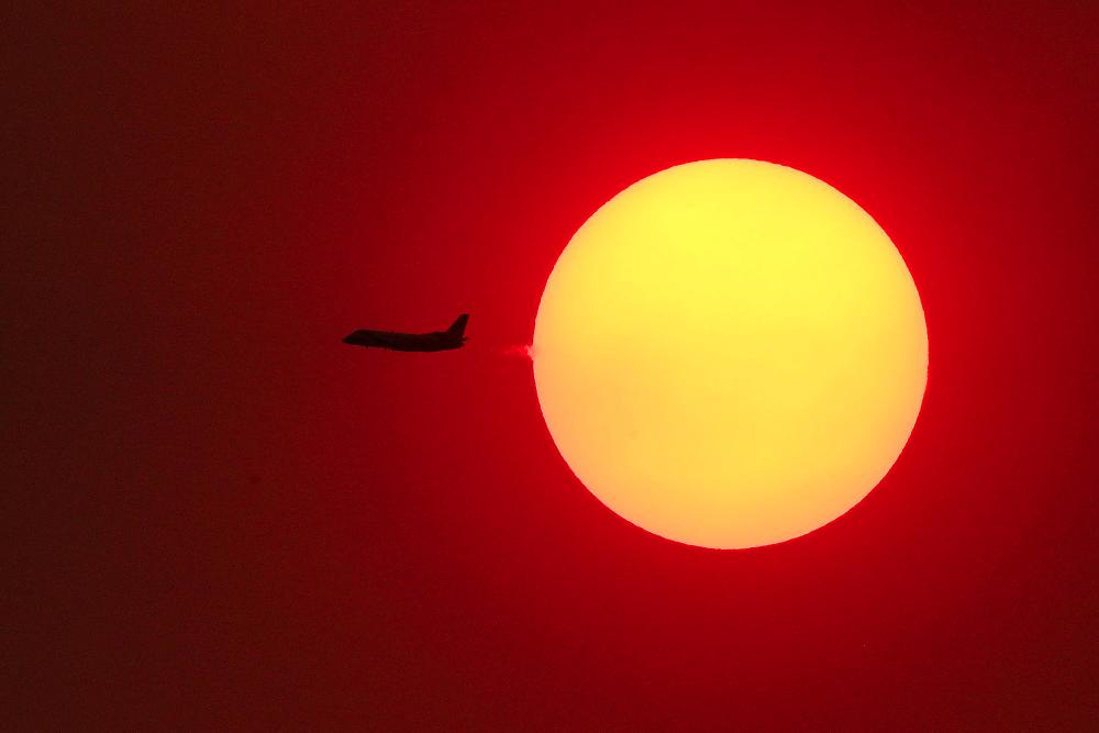 This picture taken on Dec 4, shows a passenger aircraft flying across the setting sun in Sydney, as smoke haze continues to hang over the city with more than 50 bushfires still burning across New South Wales. — AFP