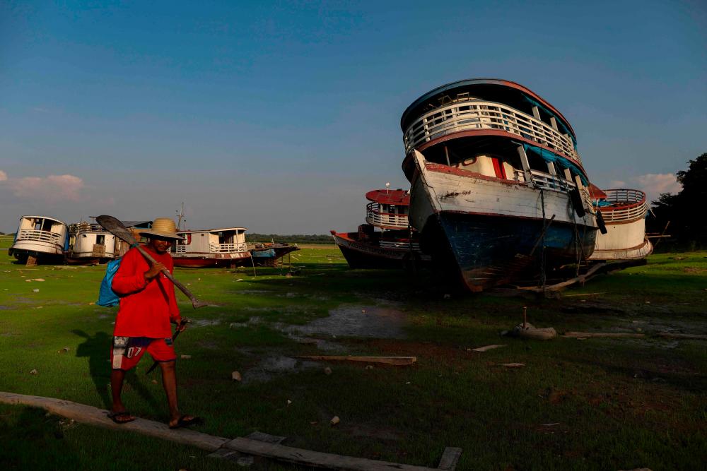 A man walks past stranded boats in Aleixo Lake due to the severe drought west of Manaus, Amazonas State, on September 29, 2023. AFPPIX