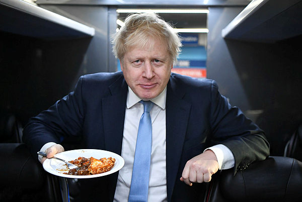 Britain’s Prime Minister Boris Johnson eats a portion of pie on the campaign bus after a visit to the Red Olive catering company in Derby, central England on Dec 11, 2019 — AFP