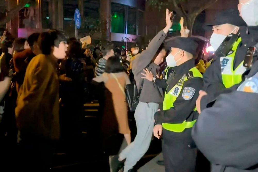 This frame grab from eyewitness video footage made available via AFPTV on November 27, 2022 shows demonstrators shouting slogans as police hold their positions, in Shanghai. AFPPIX
