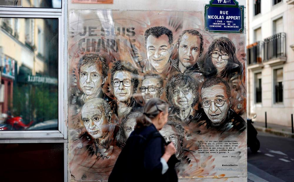 A woman walks past a painting by French street artist and painter Christian Guemy, known as C215, in tribute to members of Charlie Hebdo newspaper who were killed by jihadist gunmen in January 2015, in Paris, on August 31, 2020. — AFP