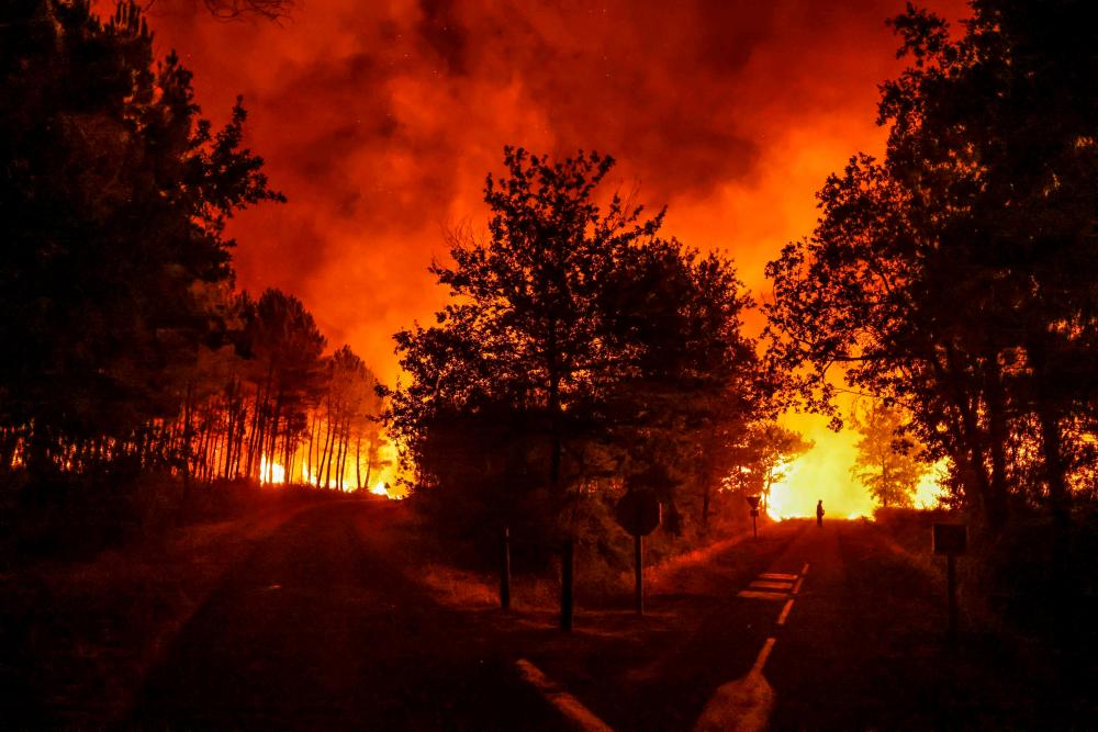 A picture taken overnight on August 11, 2022 shows a silhouette on a road near burning trees at a wildfire near Belin-Beliet, southwestern France. AFPPIX