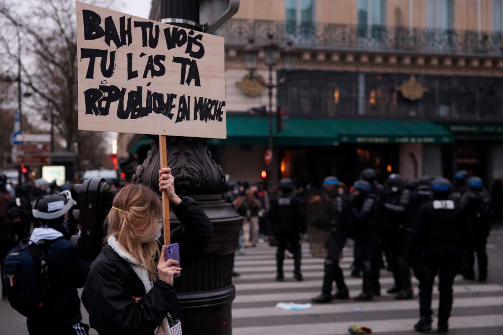 A protester (L) holds a placard redaing “well you see you have your marching republic” with French police officers in riot gear in the background (R) during a demonstration, a week after the government pushed a pensions reform through parliament without a vote, using the article 49.3 of the constitution, in Paris on March 23, 2023/AFPPix
