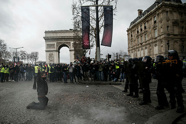 A protestor, on his knees, faces riot police officers during a “yellow vest” (gilet jaune) demonstration against rising costs of living in front of the Arc de Triomphe in Paris on Dec 8, 2018. — AFP