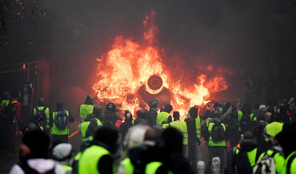Demonstrators stand in front of a burning car during a protest of Yellow vests (Gilets jaunes) against rising oil prices and living costs, on Dec 1, 2018 in Paris. — AFP