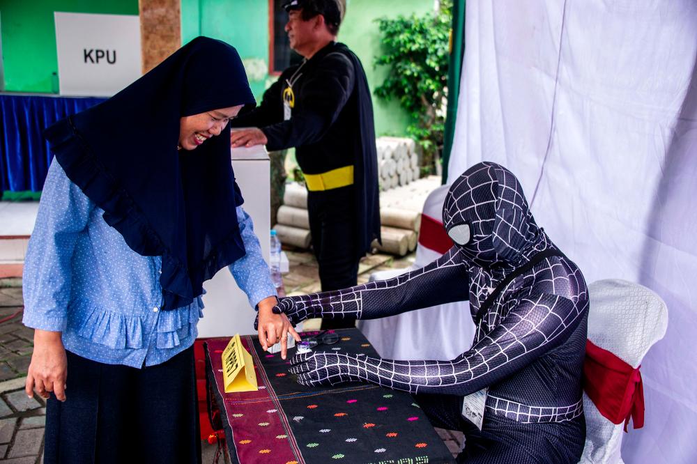 Indonesian election workers dressed in superhero costumes register voters at a polling station in Surabaya on April 17, 2019. — AFP