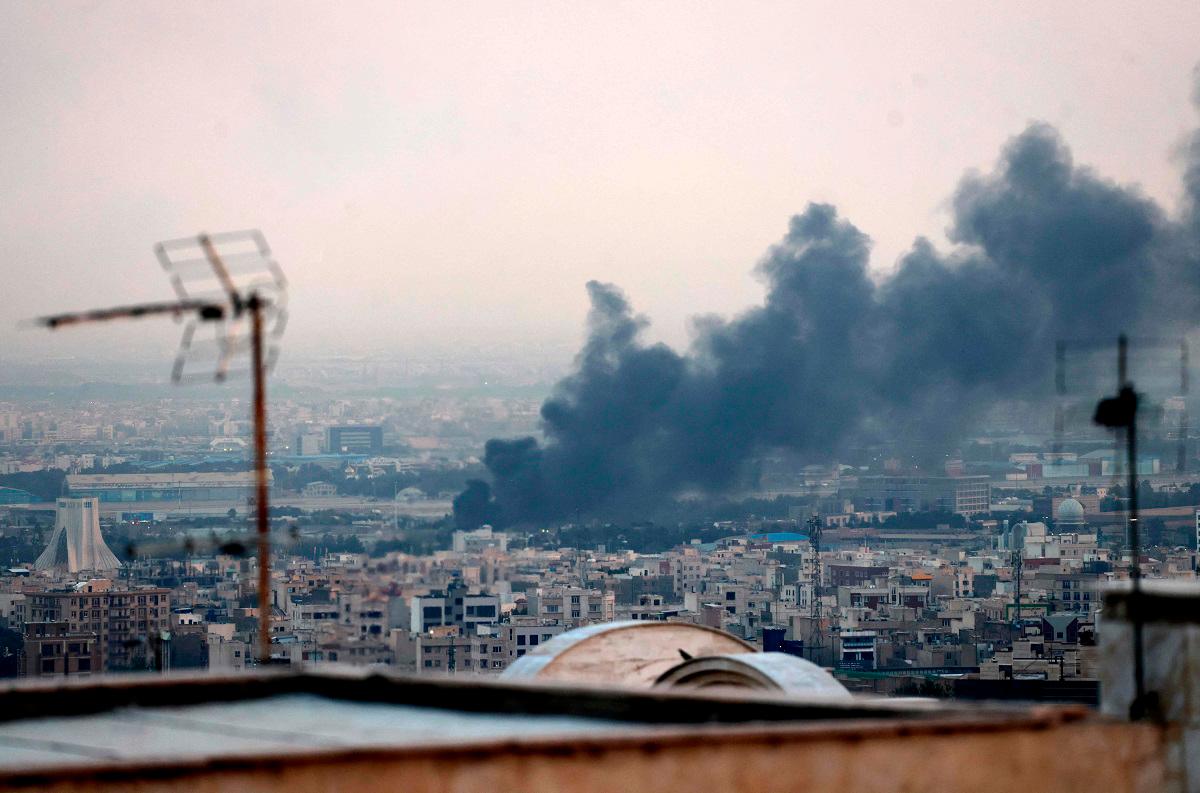 Smoke billows from an explosion near the Azadi Tower (L) in Tehran on June 16, 2025. The Islamic Republic of Iran Broadcasting (IRIB) building was struck in an Israeli attack on June 16, cutting live coverage immediately. The blast occurred as the presenter was live on TV lambasting Israel before she was seen leaving the live broadcast, Iranian media reported, sharing a video of the incident. - ATTA KENARE / AFP