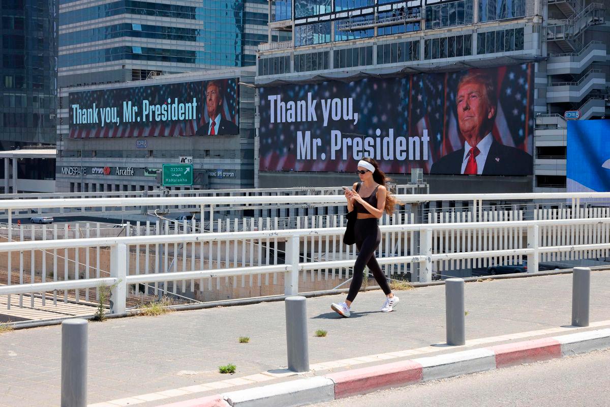A woman walks on a bridge in front of banners bearing a pictures of US President Donald Trump accompanied by a messages, in Tel Aviv on June 22, 2025. (Photo by AHMAD GHARABLI / AFP)
