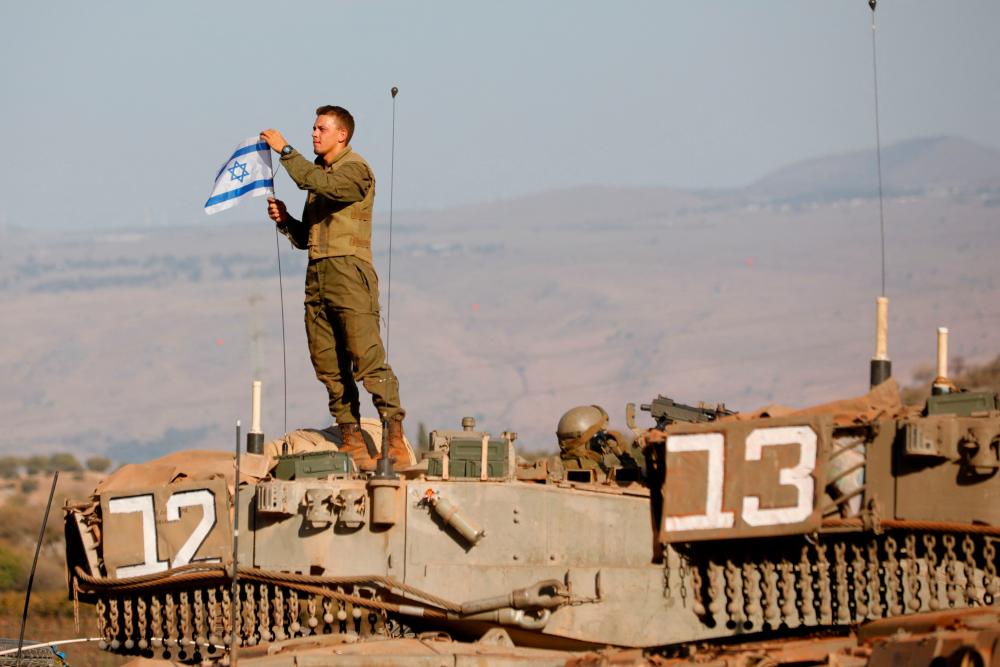 An Israeli soldier places a national flag atop a Merkava tank during in a military drill near the border with Lebanon in the upper Galilee region of northern Israel on October 26, 2023, amid the ongoing battles between Israel and the Palestinian group Hamas in the Gaza Strip. AFPPIX