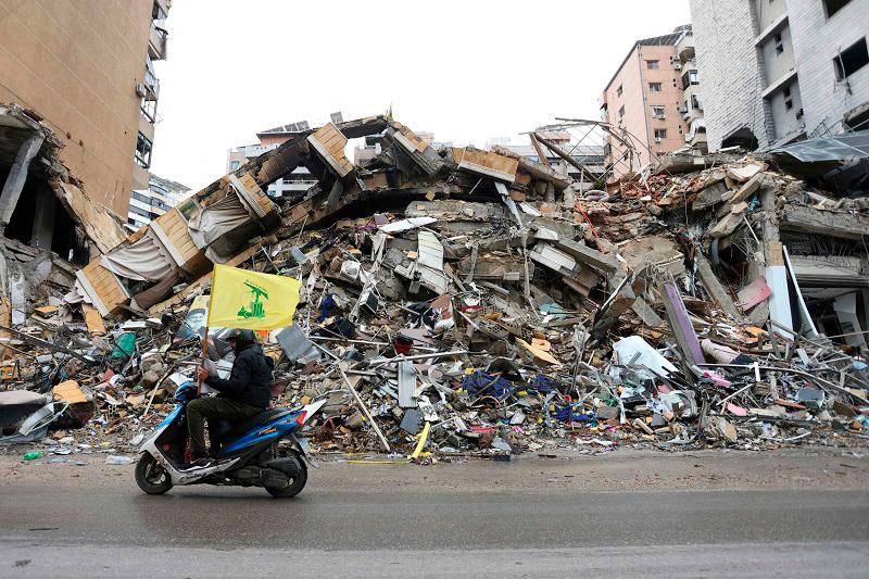 A man waves the flag of Hezbollah as he drives past the rubble of a building in Beirut’s southern suburbs on November 27, 2024, as people returned to the area to check their homes after a ceasefire between Israel and Hezbollah took effect. A ceasefire between Israel and Hezbollah in Lebanon took hold on after more than a year of fighting that has killed thousands. - IBRAHIM AMRO / AFP