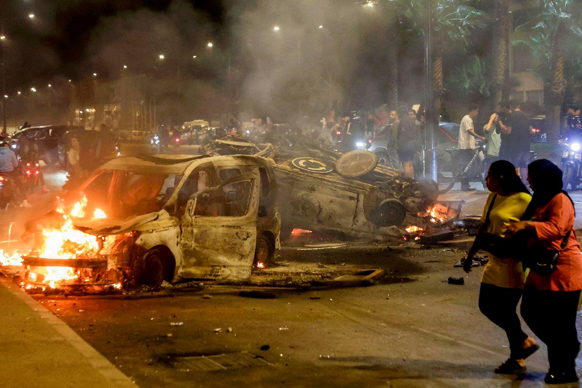 Women walk past police vehicles set on fire during a youth-led demonstration demanding reforms in the healthcare and education sectors in Sale on October 1, 2025. (Photo by Abdel Majid BZIOUAT / AFP)