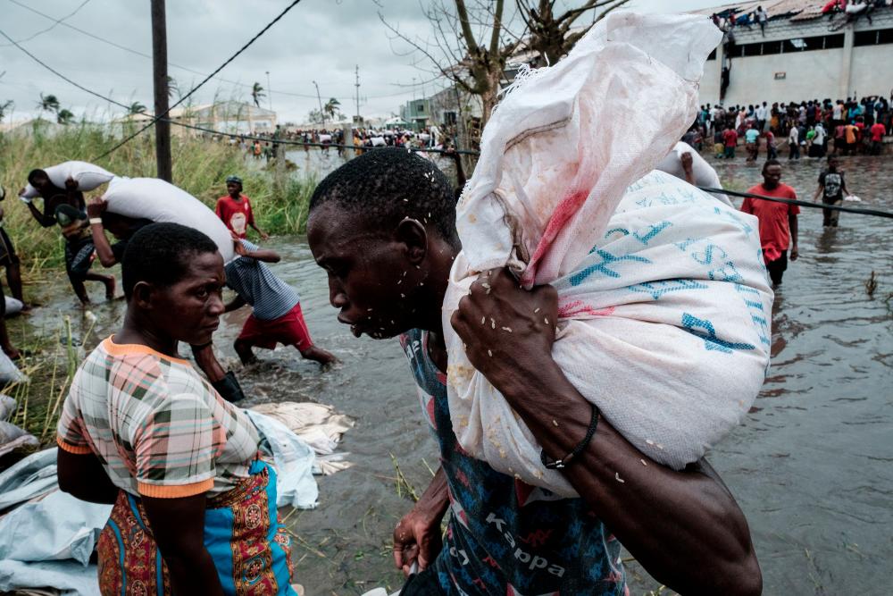 People take part in the looting sacks of Chinese rice printed China Aid from a warehouse which is surrounded by water after cyclone hit in Beira, Mozambique, on March 20, 2019. Five days after tropical cyclone Idai cut a swathe through Mozambique, Zimbabwe and Malawi, the confirmed death toll stood at more than 300 and hundreds of thousands of lives were at risk, officials said. — AFP