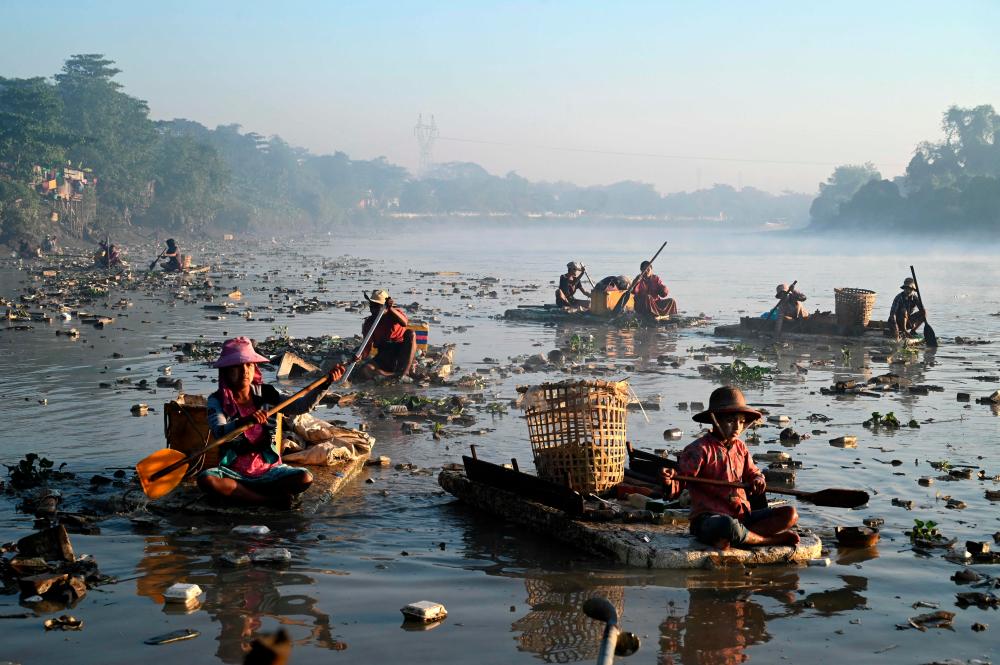This photo taken on January 14, 2023 shows waste collectors paddling polystyrene boats as they look for plastic and glass to recycle in Pazundaung Creek in Yangon. AFPPIX