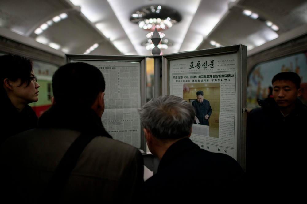 Commuters read the Rodong Sinmun newspaper showing an image of North Korea's leader Kim Jong Un casting his ballot at the 14th Supreme People's Assembly elections, on display at a subway station in Pyongyang on March 11, 2019. — AFP