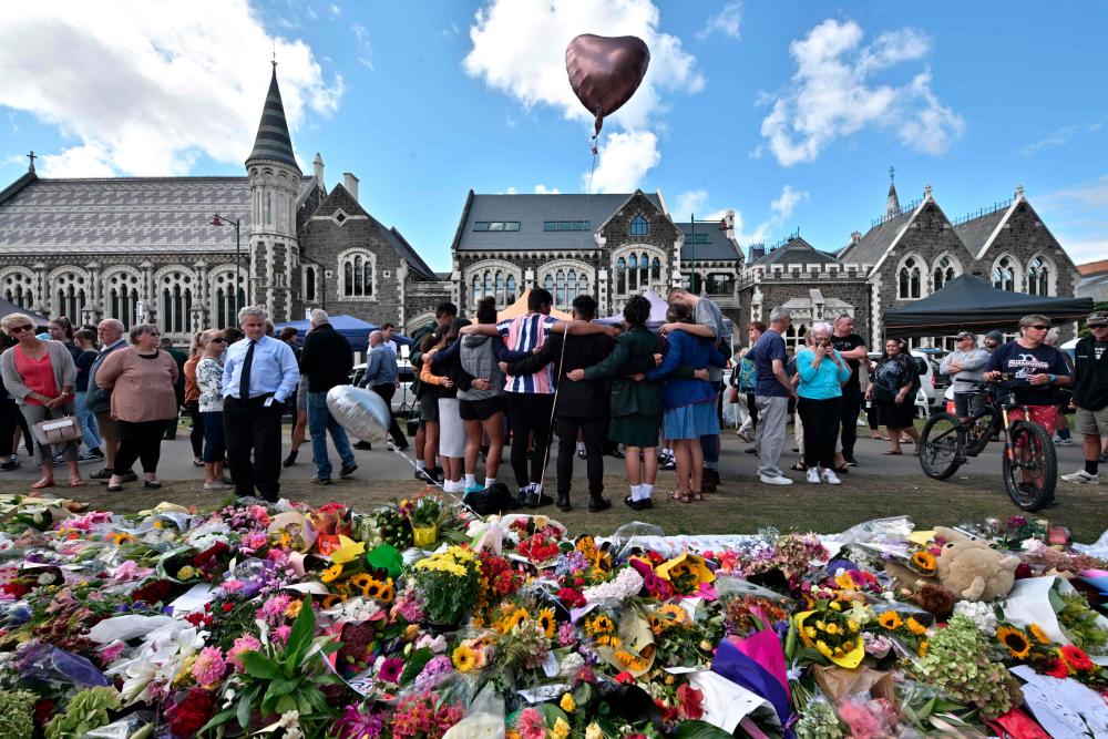 A group of students (C) sings in front of flowers left in tribute to victims at the Botanical Garden in Christchurch on March 19, 2019, four days after a shooting incident at two mosques that claimed the lives of 50 people. — AFP