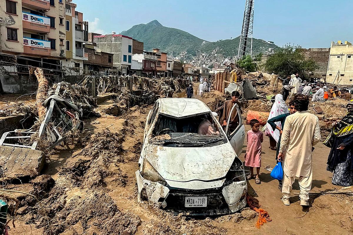 People gather near a damaged vehicle and scattered debris after the road washed out following a flash flood in Mingora, the main city of Swat Valley, in monsoon-hit northern Pakistan’s mountainous Khyber Pakhtunkhwa province on August 16, 2025. The death toll from heavy monsoon rains that have triggered flash floods across northern Pakistan has risen to at least 321 people in the last 48 hours, disaster agencies said on August 16. - Mehboob UL HAQ / AFP