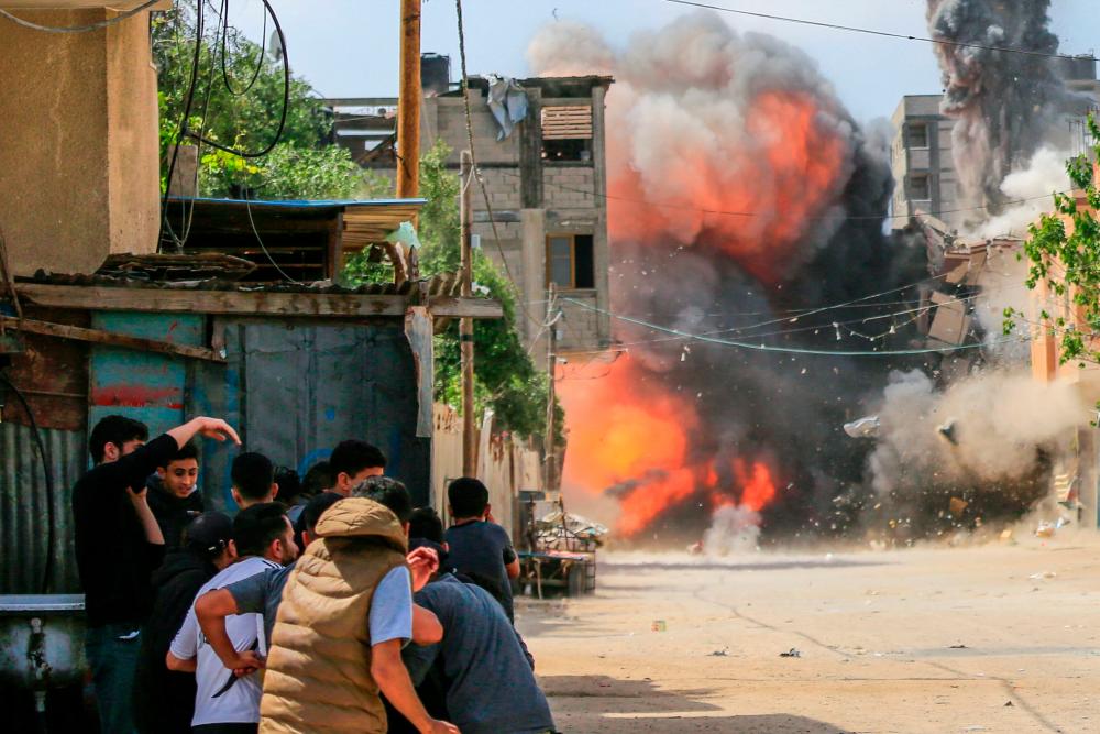 People take cover as a building is hit by an Israeli air strike in Beit Lahia, northern Gaza Strip, on May 12, 2023. AFPPIX