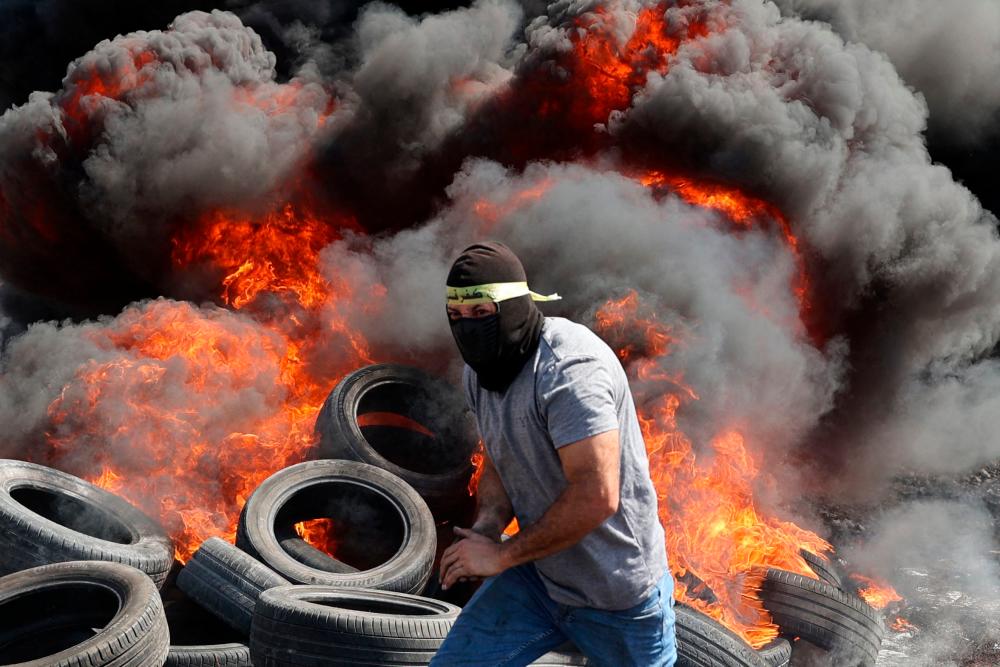 TOPSHOT - A protester runs near burning tyres during clashes with Israeli forces following a demonstration against the expropriation of Palestinian land by Israel in the village of Kfar Qaddum, in the occupied West Bank on September 29, 2023. AFPPIX