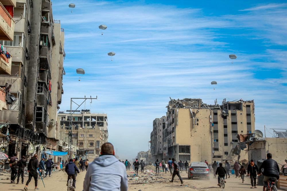 Palestinians run along a street as humanitarian aid is airdropped in Gaza City on March 1, 2024, amid the ongoing conflict between Israel and the Hamas militant group/AFPPix