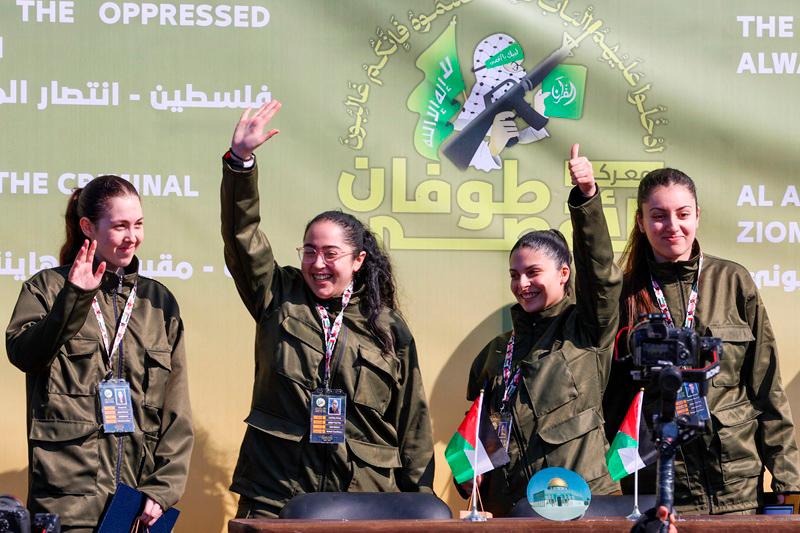 Four Israeli hostages wave on a stage before Hamas fighters hand them over to a team from the Red Cross in Gaza City on January 25, 2025. Hamas militants handed over four Israeli women hostages to the Red Cross in a January 25 swap after parading them on a stage at a square in Gaza, an AFP journalist reported. - Omar AL-QATTAA / AFP