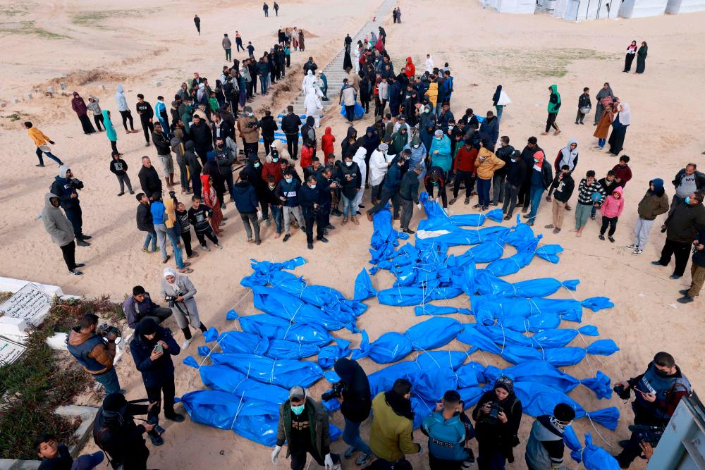 Civilians watch as Gaza-based Palestinian Health Ministry workers bury the bodies of unidentified Palestinians whose date of death is not known after they were returned by Israel earlier on the same day through the Kerem Shalom crossing, at a mass grave east of Rafah in the southern Gaza Strip on January 30, 2024, amid the ongoing conflict between Israel and the Palestinian militant group Hamas. Palestinians buried dozens of bodies in a mass grave in southern Rafah, after Gaza officials said Israel returned the remains of people it had exhumed from the territory/AFPPix