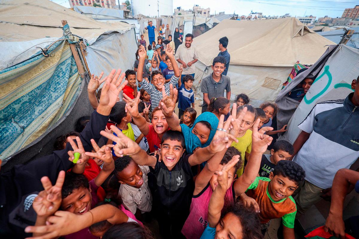 Palestinian children celebrate at a camp for displaced people in Nuseirat in the central Gaza Strip on October 9, 2025, following news of a new Gaza ceasefire deal. - Eyad BABA / AFP