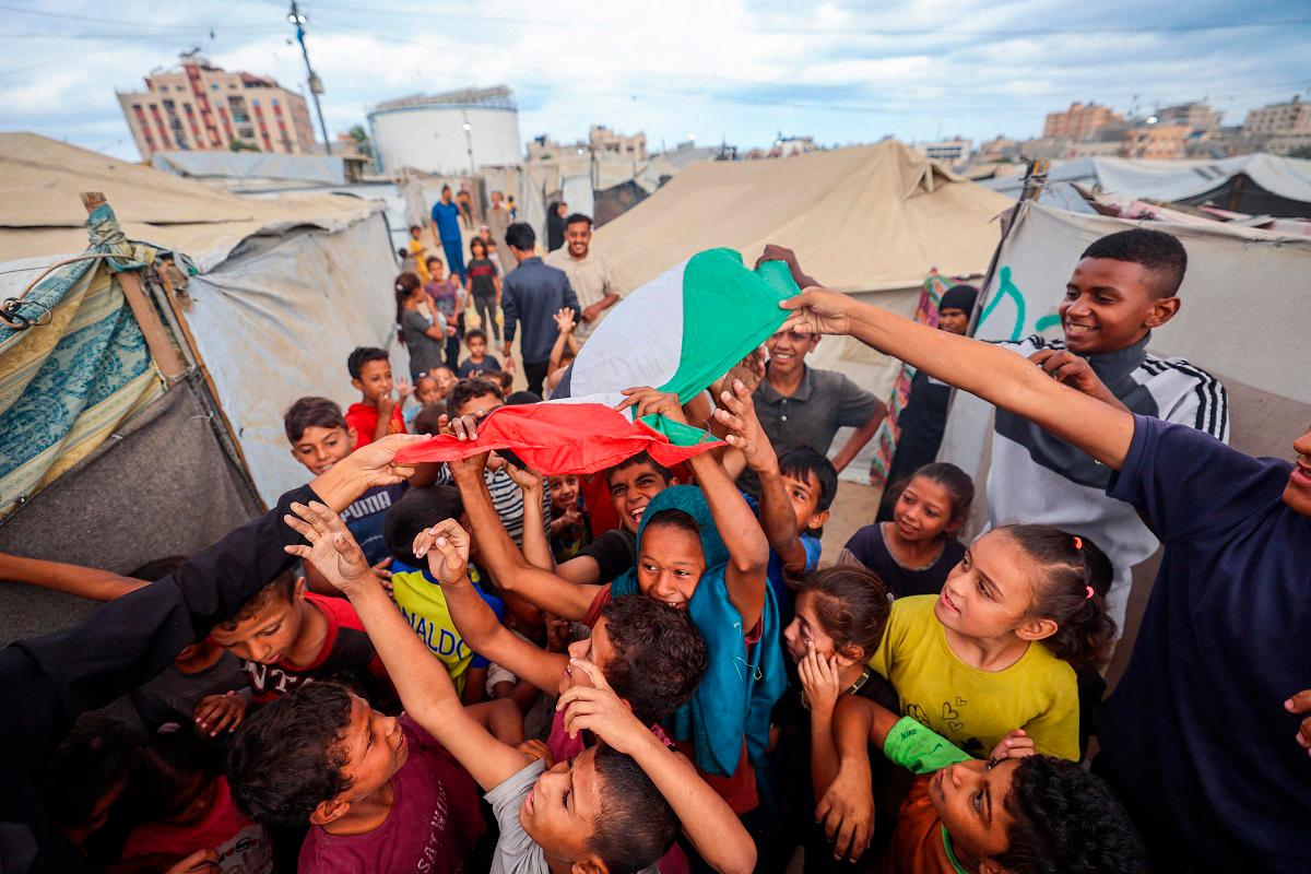 Palestinian children celebrate at a camp for displaced people in Nuseirat in the central Gaza Strip on October 9, 2025, following news of a new Gaza ceasefire deal. - Eyad BABA / AFP