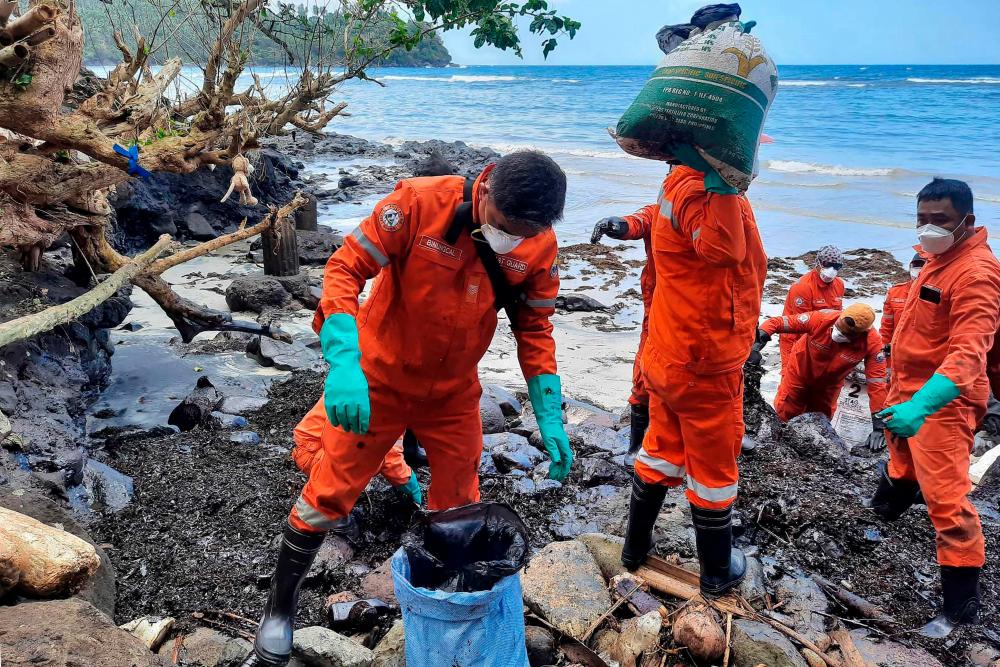 This handout photo taken on March 8, 2023 and released by the Philippine Coast Guard (PCG) shows coast guard personnel and volunteers collecting debris covered with oil during a clean-up along the coast in Pola, Oriental Mindoro Province, days after an oil spill from a sunken tanker. AFPPIX