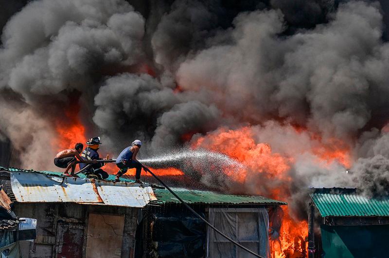 Residents and firefighters put out a fire at Tondo in Manila on November 24, 2024. Raging orange flames and thick black smoke billowed into the sky, as fire ripped through hundreds of houses in a closely built slum area of the Philippine capital Manila. - JAM STA ROSA / AFP