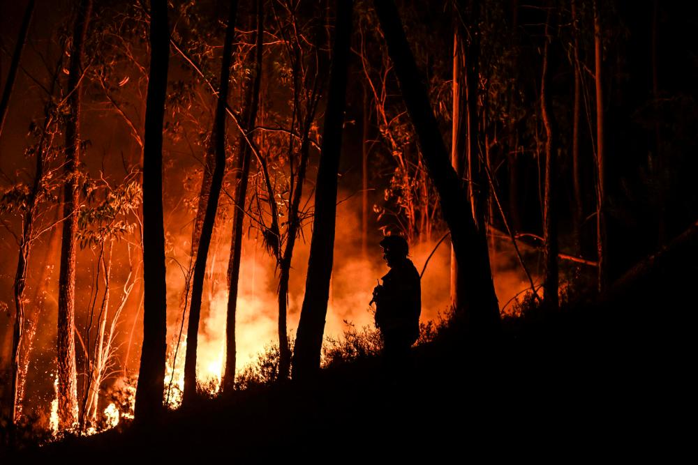 A silhouette of a firefighter standing in the forest is pictured during a wildfire at Casais do Vento in Alvaiazere on July 10, 2022. AFPPIX