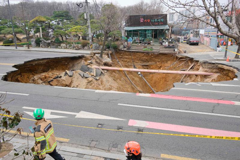 Rescue workers walk past a sinkhole outside a plant shop on a road in Seoul on March 25, 2025. One person has been killed after a massive sinkhole opened up in Seoul, AFPpix